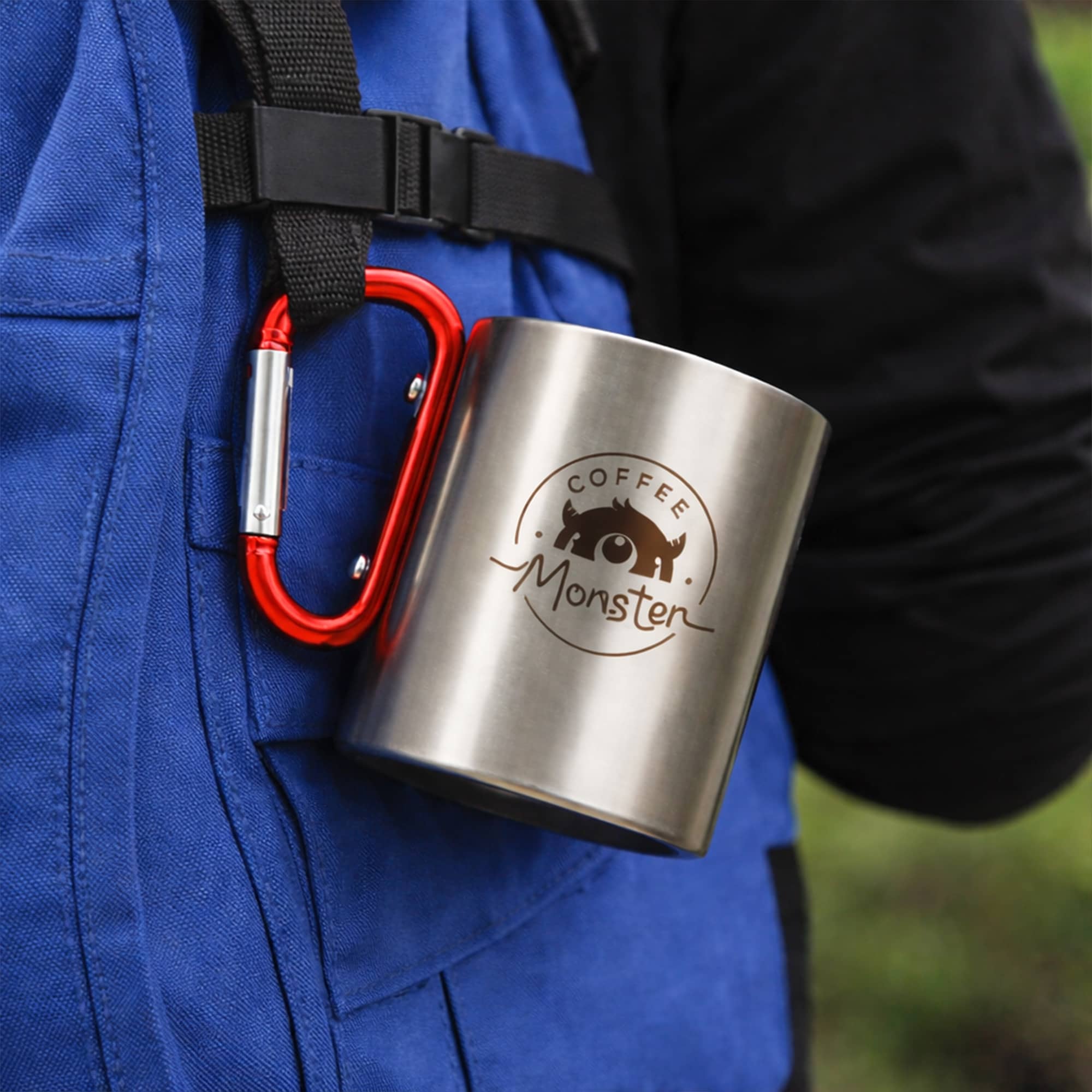 A stainless steel insulated travel mug, silver in colour, attached with a red carabiner handle.