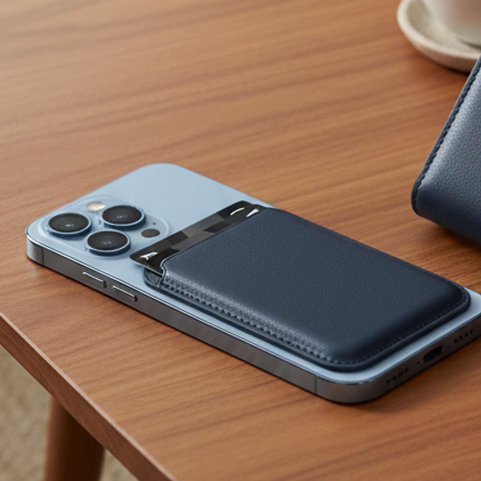 A navy PU magnetic phone card holder attached to a light blue smartphone, resting on a wooden table.