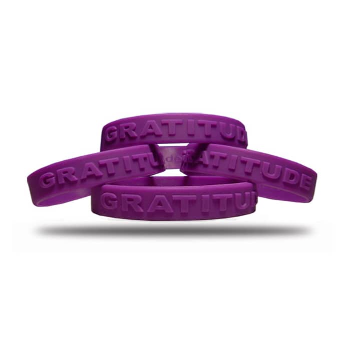 Four purple embossed wristbands stacked together, featuring an embossed gratitude message and a logo.