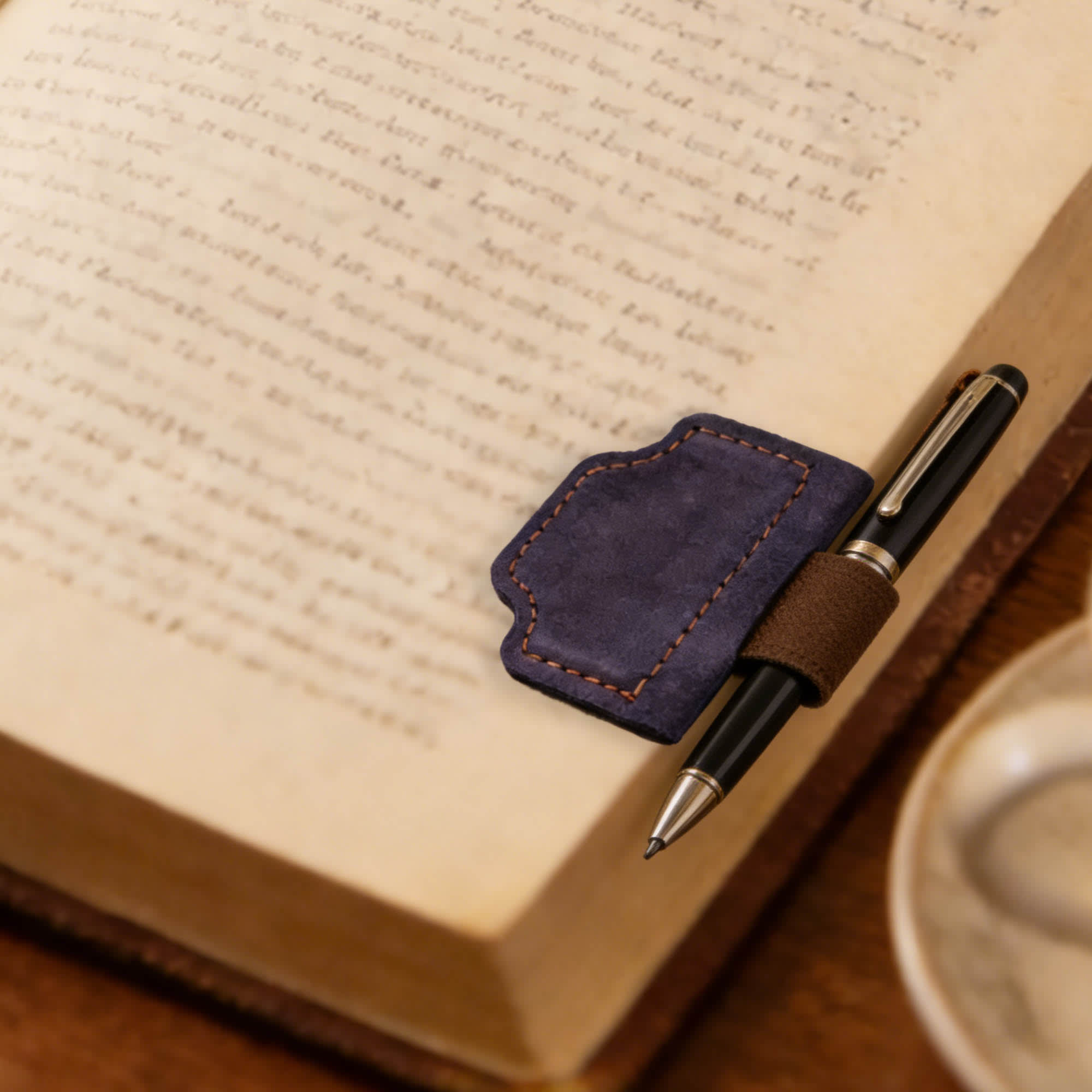 A navy blue magnetic bookmark with a pen clip resting on an open book, with a pen attached for convenience.