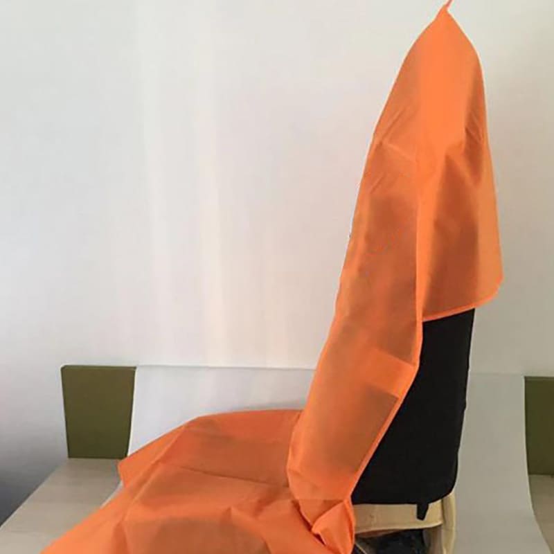 An orange non-woven car seat cover draped over a black chair, featuring a branding logo.