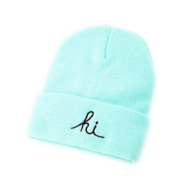 A mint green knitted beanie with a black embroidered message and a logo on the band.
