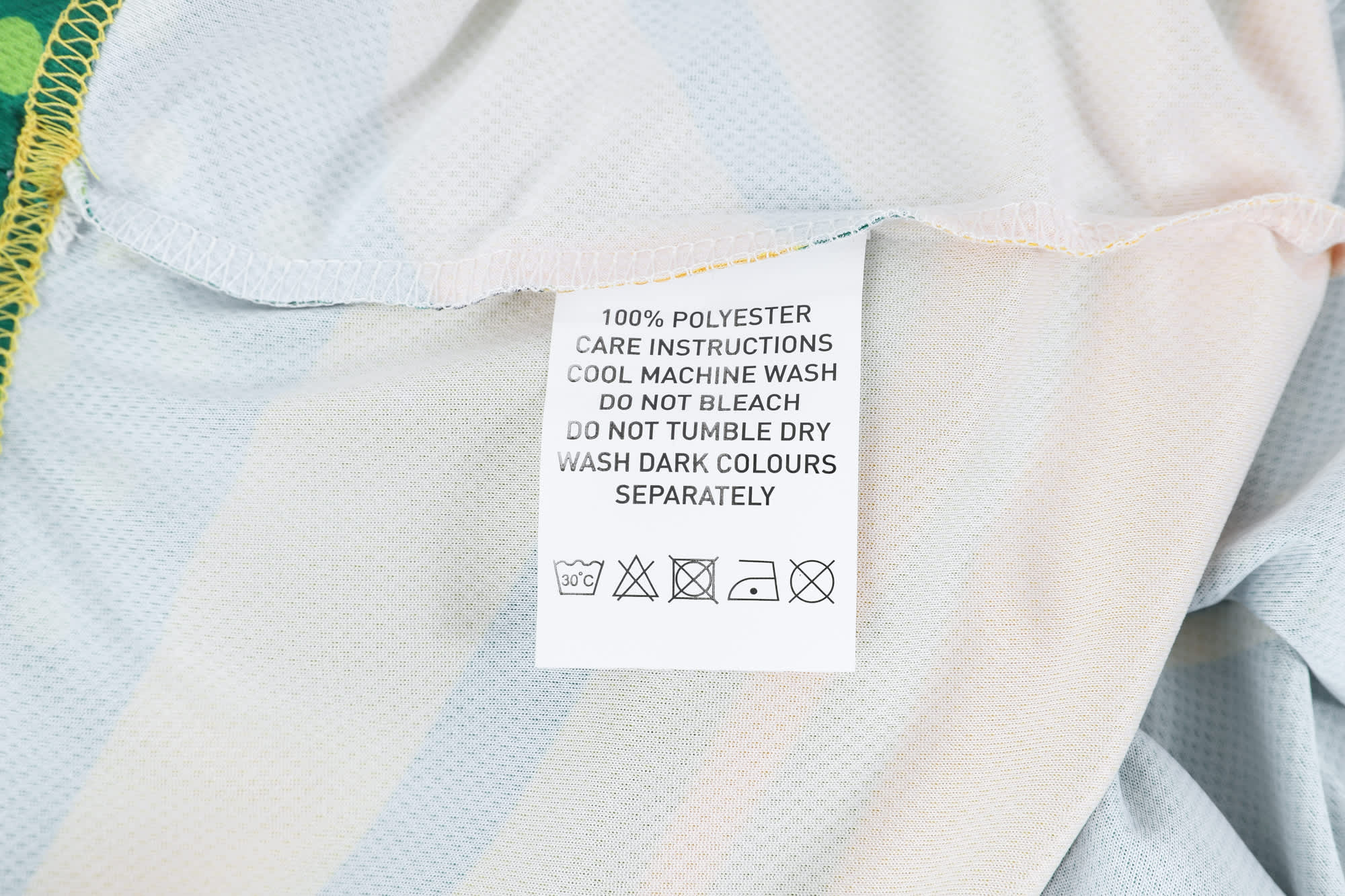 A care label on a 100% polyester micro mesh sports long sleeves shirt, featuring fabric care instructions.