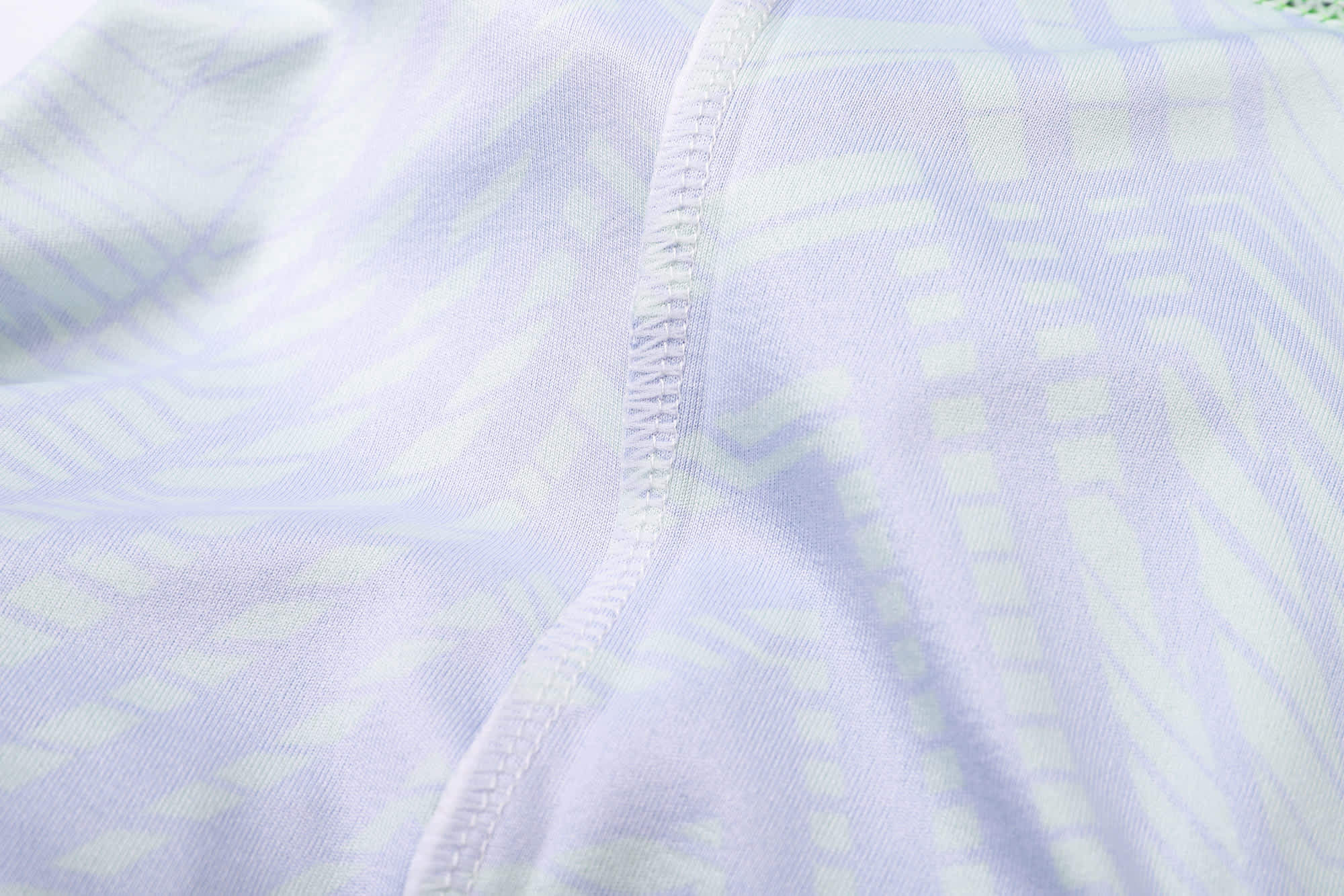 A close-up of a light-coloured, patterned fabric showcasing stitching details of a V-neck shirt.