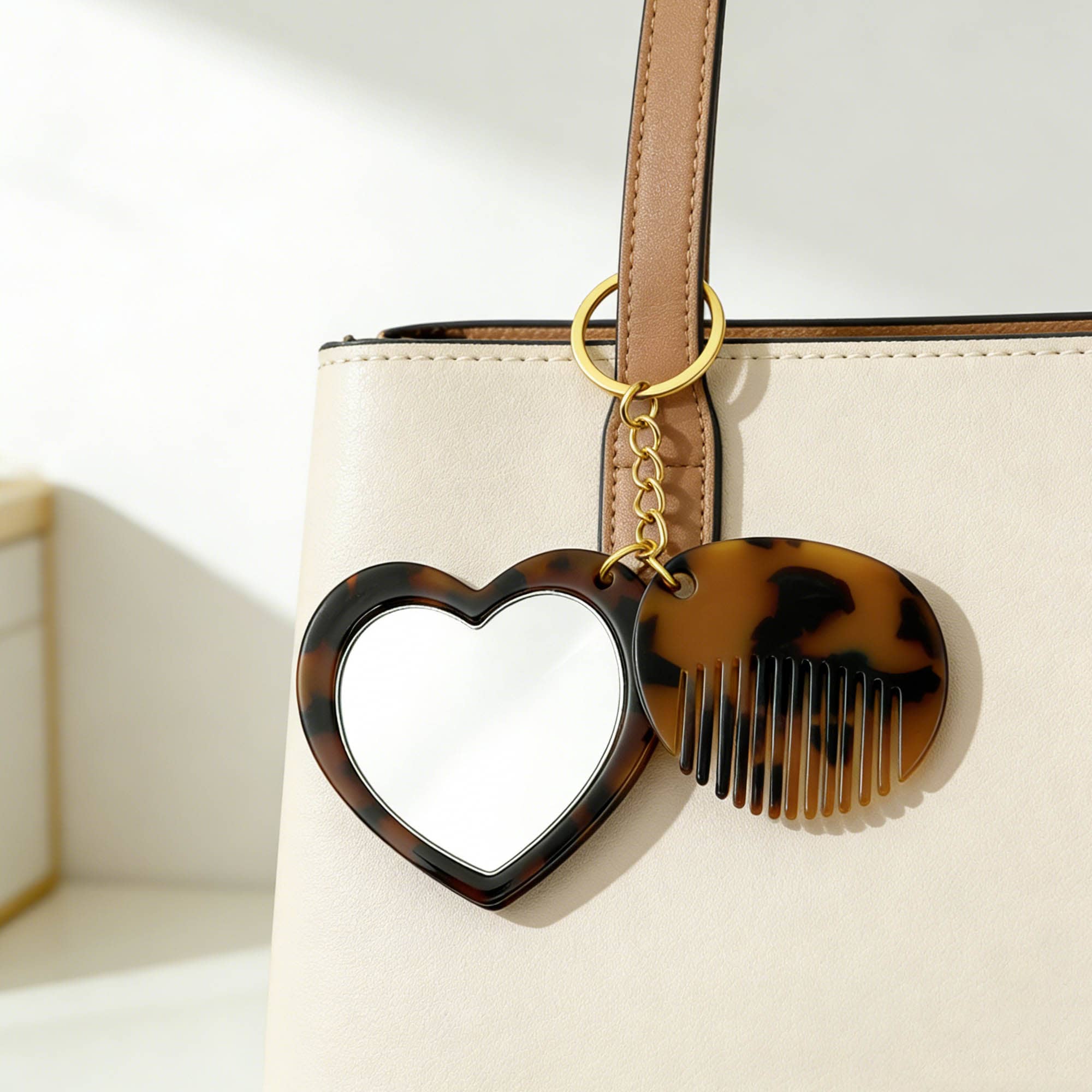A heart-shaped mirror and a comb keyring in tortoiseshell design, attached to a light-coloured handbag.