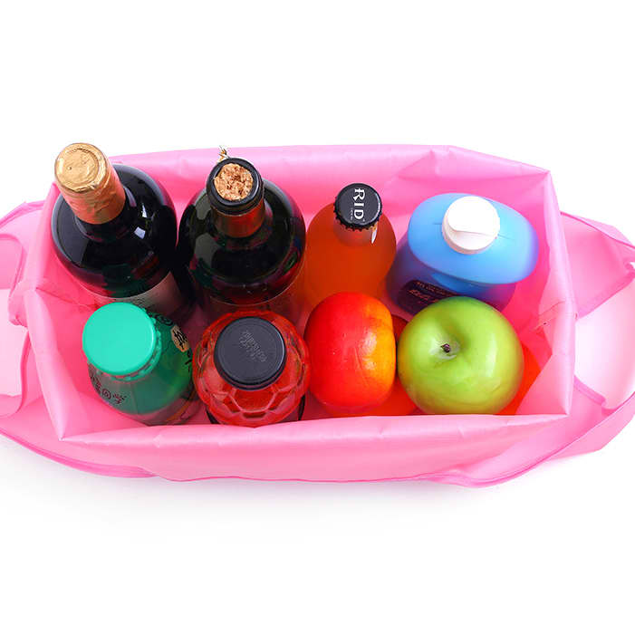 A pink reusable foldaway shopping bag filled with various bottles and two apples, one red and one green.