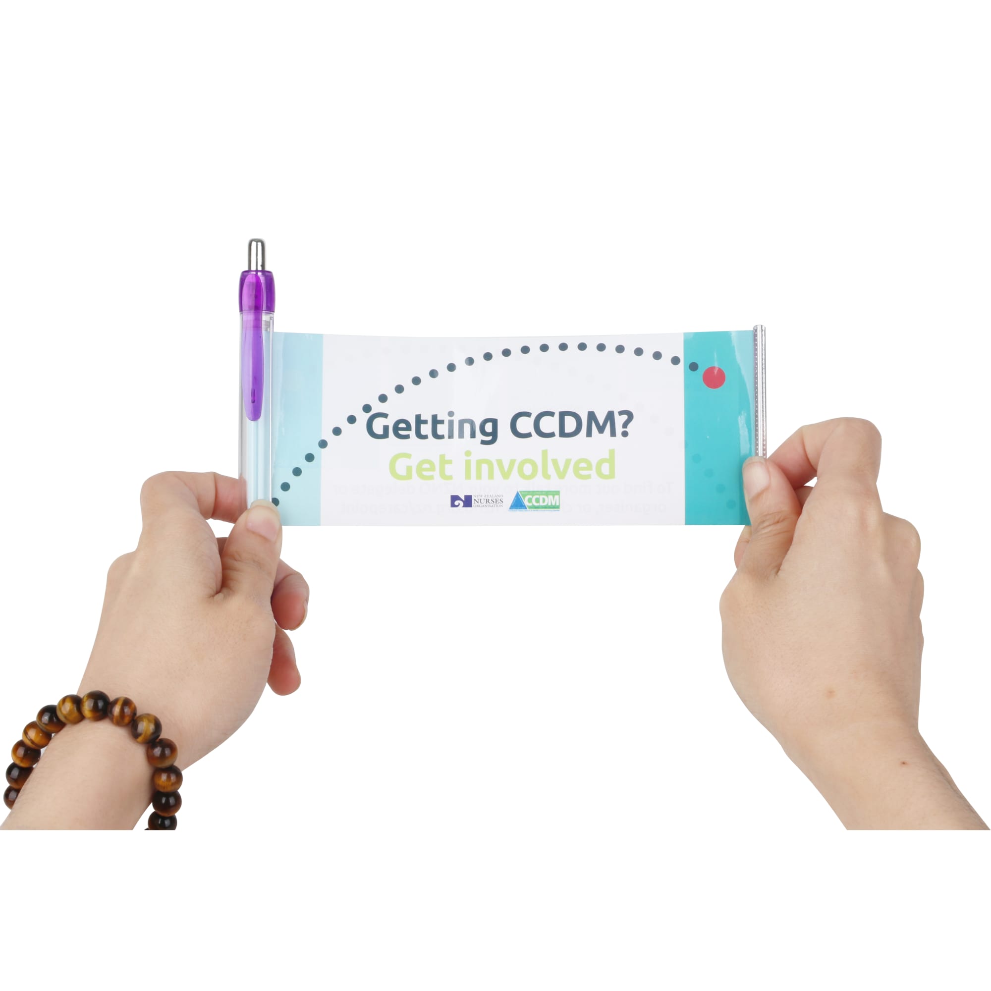A hands holding a promotional banner with a purple plastic pen attached, featuring a logo and colourful design.