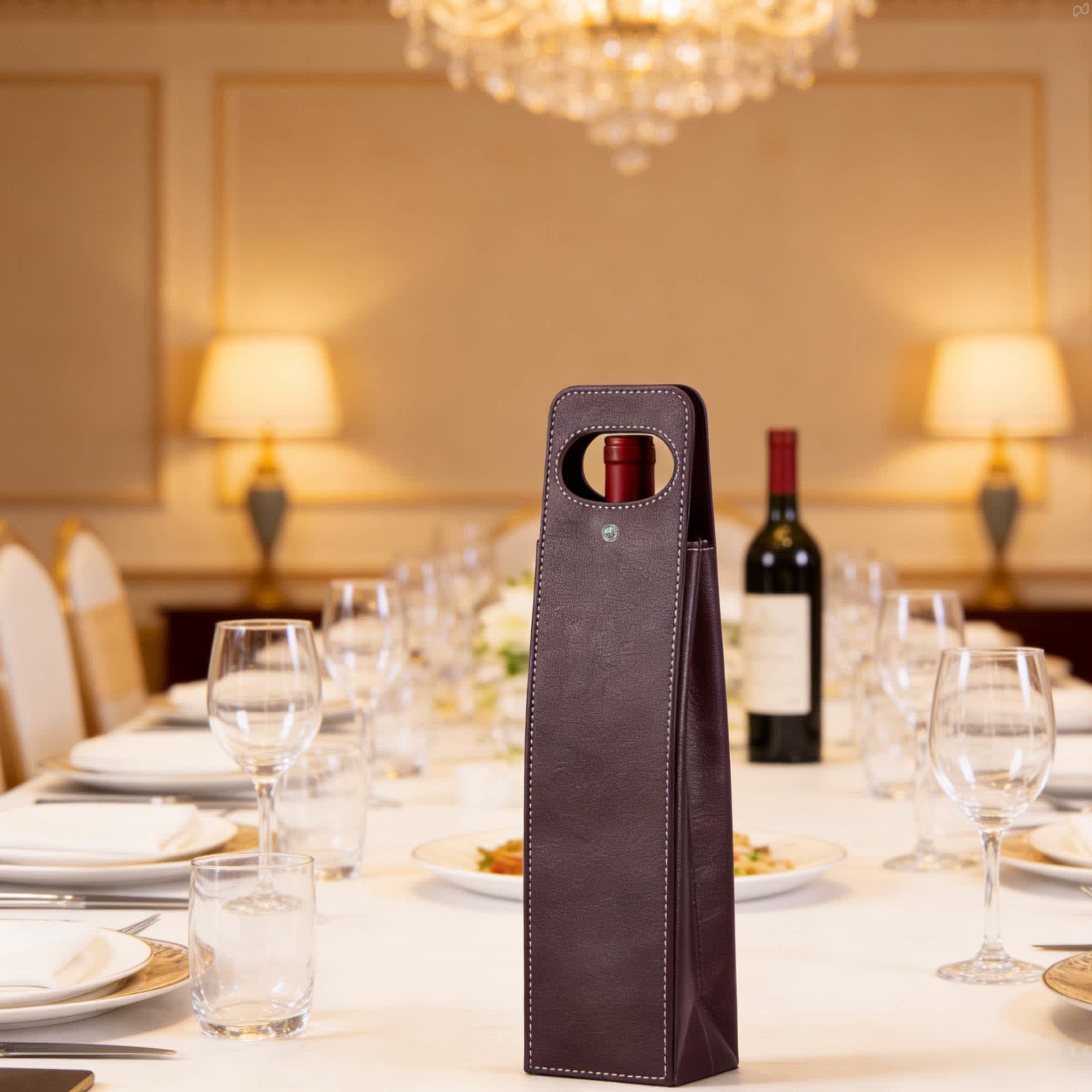 A drink bottle bag in dark burgundy with a handle, set against an elegant dining table.