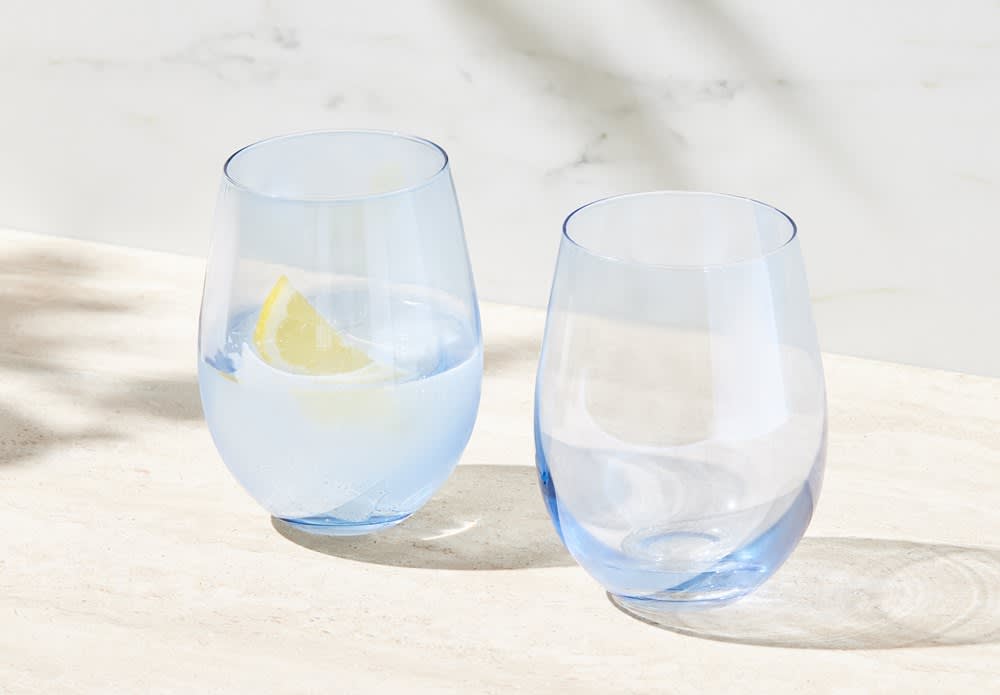 A set of two stemless wine glasses in pale blue, one filled with water and a slice of lemon.