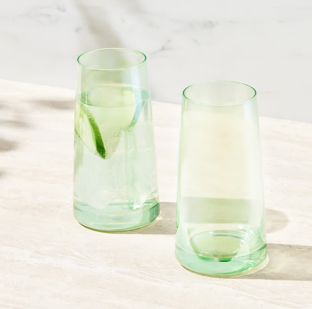 Two green highball glasses, one filled with a drink and garnished with lime, set against a light surface.