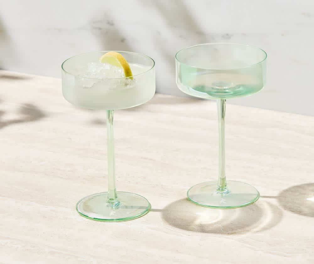 A set of two glass coupe cocktail glasses in a soft green hue, presented in a gift box.