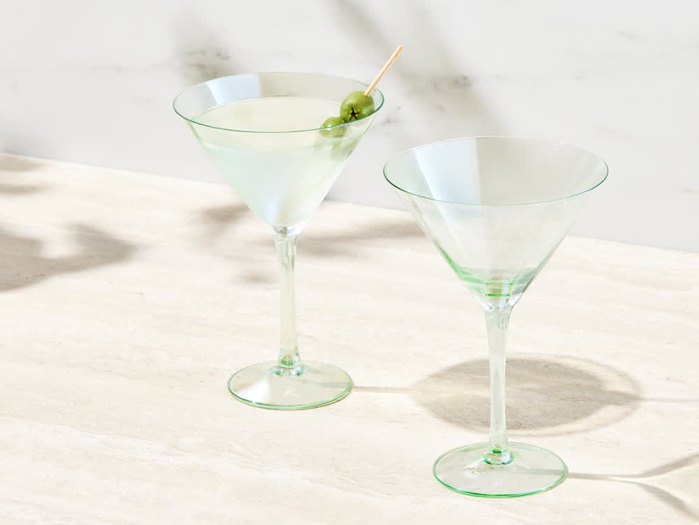 A set of two clear glass glamour martini glasses with green accents, featuring a cocktail garnished with an olive.