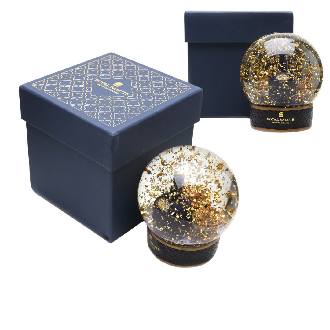 A custom snow globe with a gold glitter design, presented with a navy blue box featuring a logo.