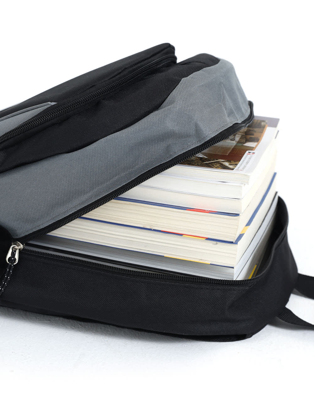 A black and grey backpack partially open, revealing several stacked books inside. It features a logo on the exterior.