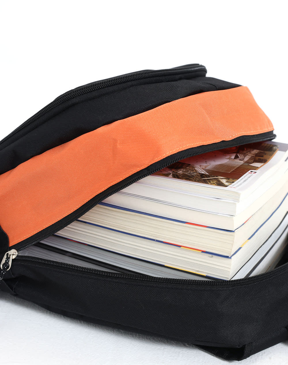A black backpack with an orange accent unzipped to reveal stacked magazines inside.