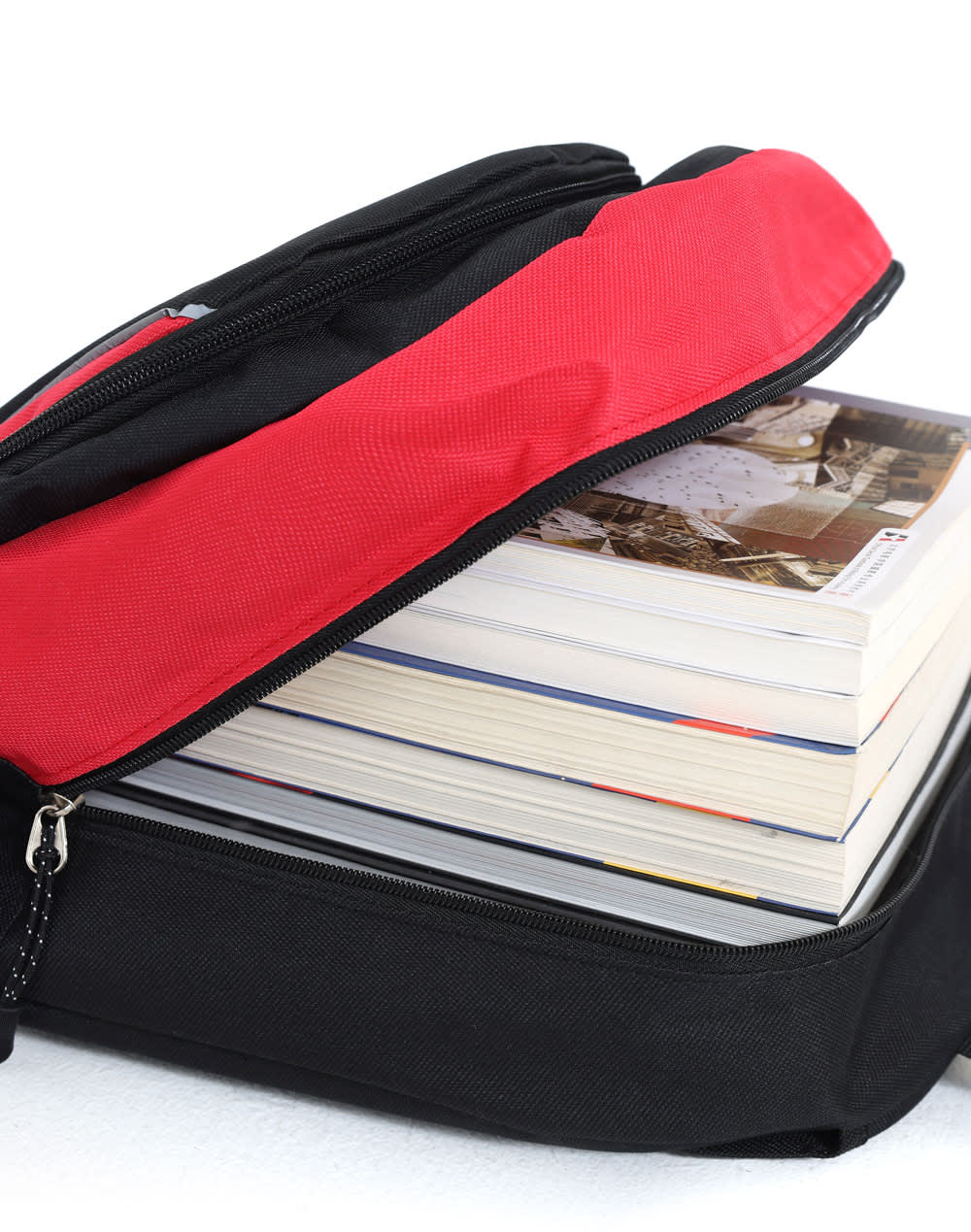 A black and red backpack with a partially opened zipper, revealing several stacked books inside.