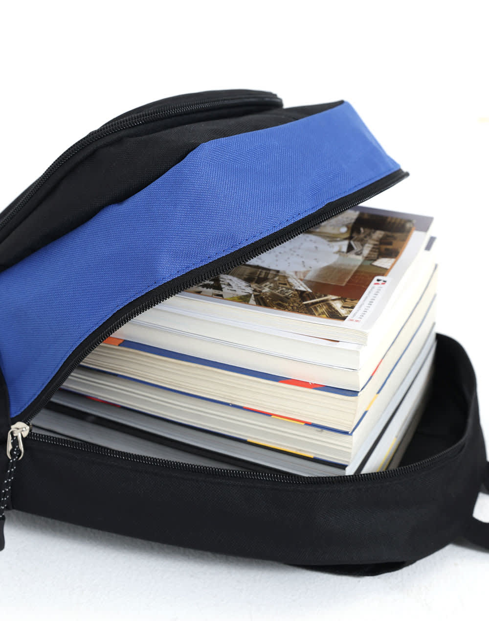 A black and blue backpack with a zippered opening, filled with several stacked books.