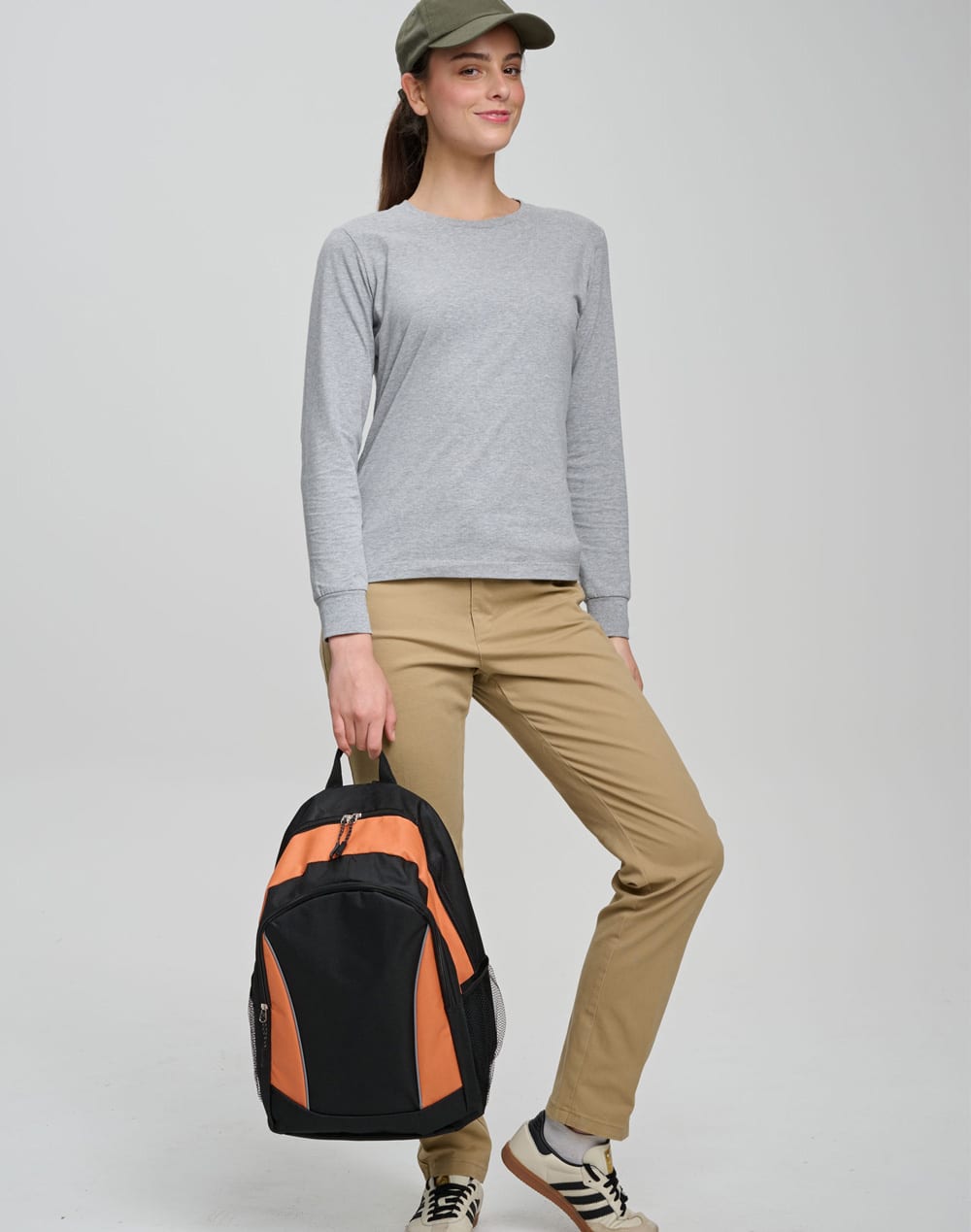 A woman wearing a grey top and khaki pants holds a black and orange Iconic Promo Backpack.