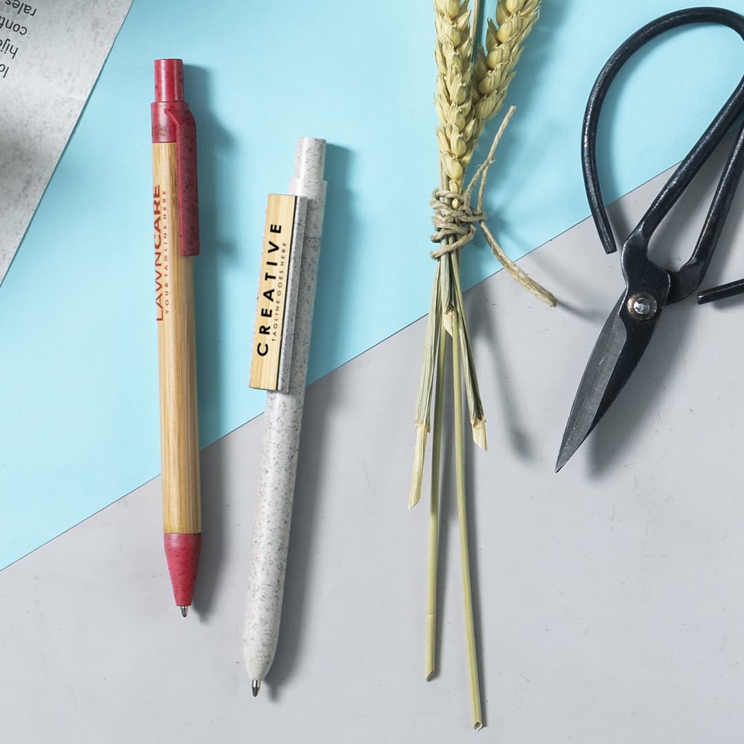 A collection of pens in red and grey, accompanied by dried wheat and scissors on a blue and grey background.