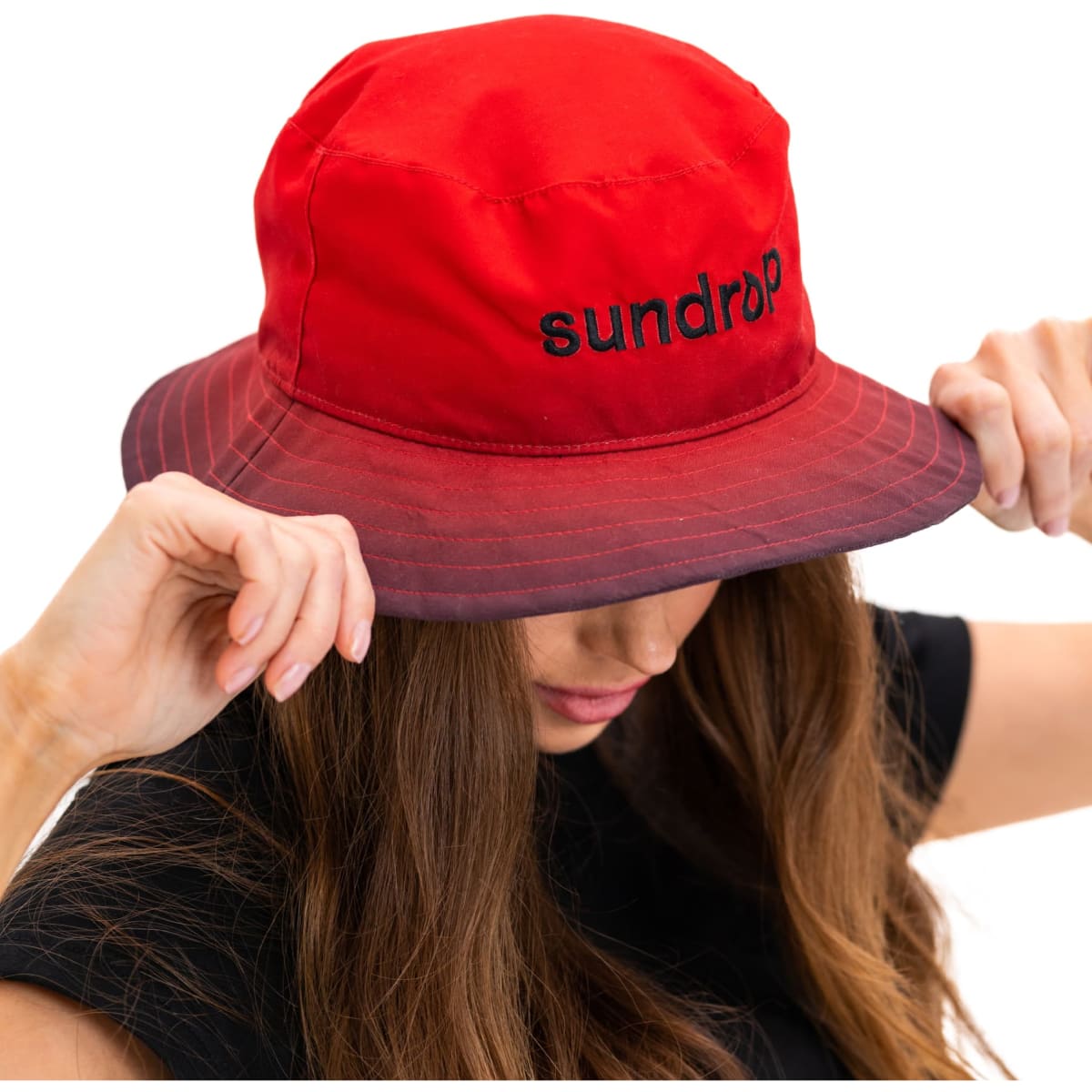 A red bucket hat with a logo, featuring a wide brim and a stylish design held by a person.