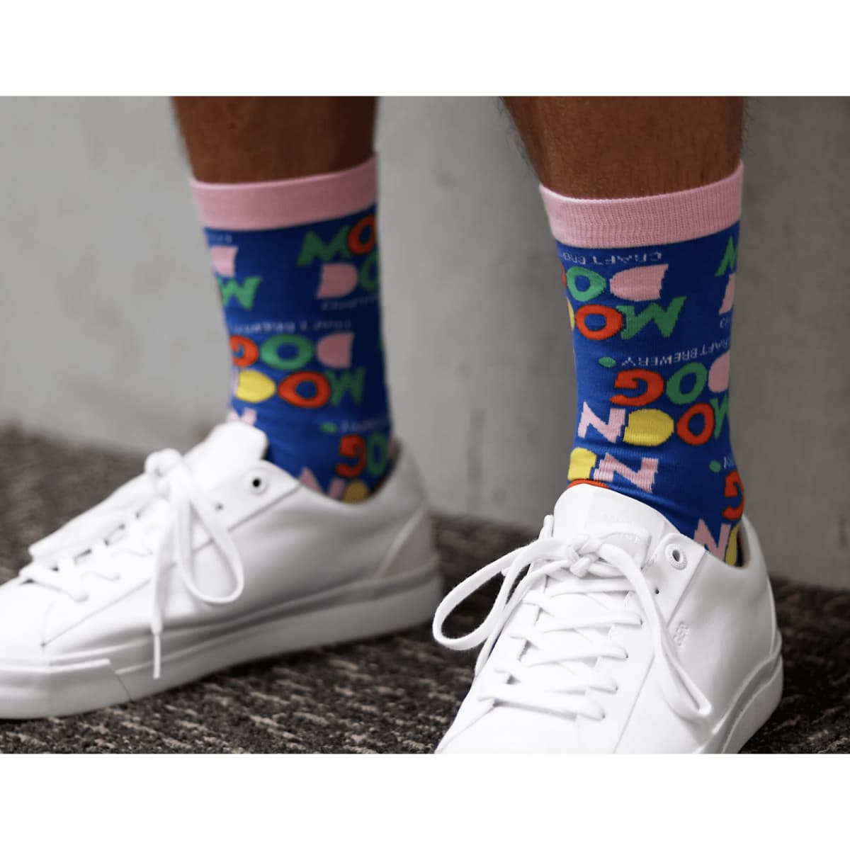 Brightly coloured socks featuring playful graphics and a pink band, worn with white sneakers on a textured surface.