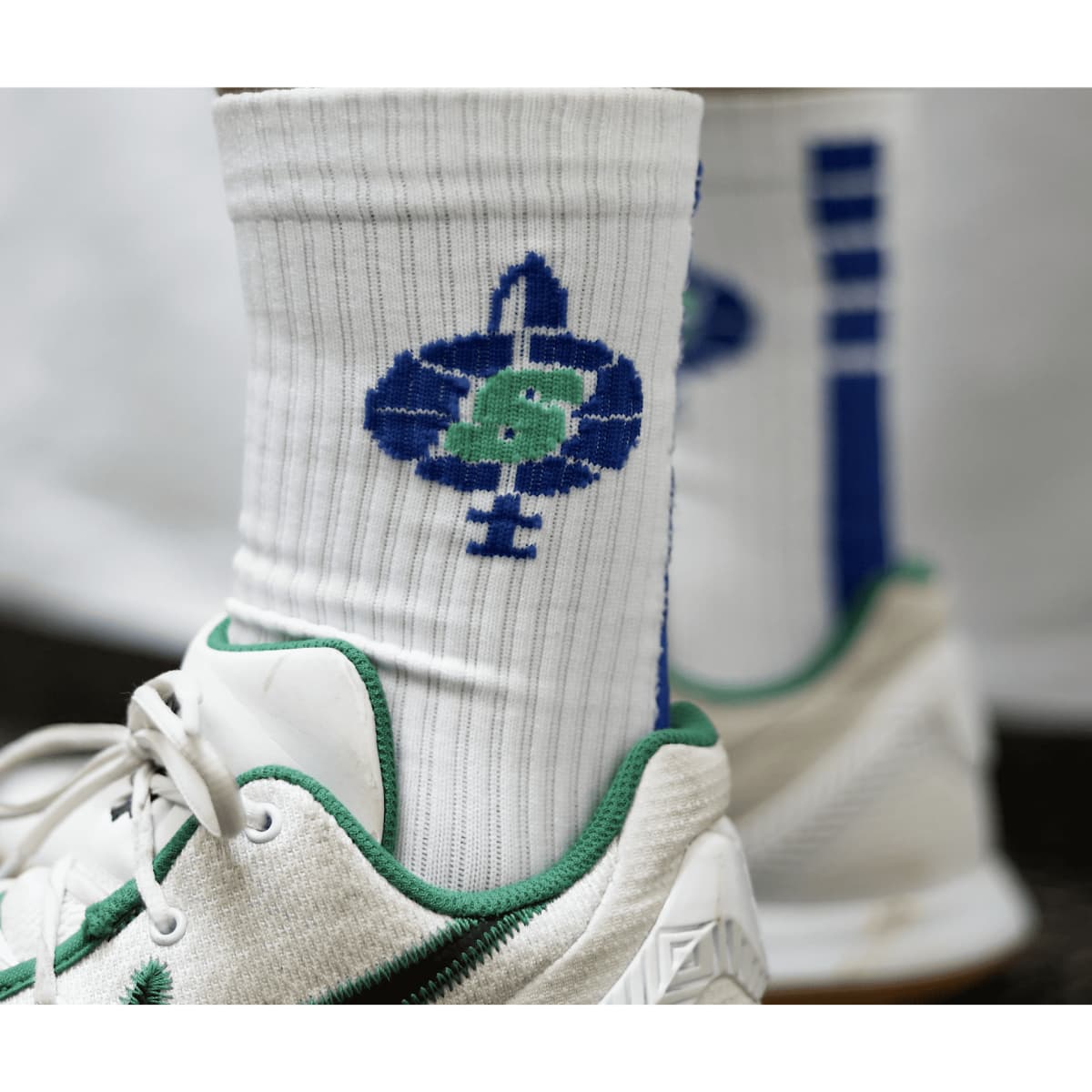 White sports socks with blue and green design, featuring a logo, paired with grey and green athletic shoes.