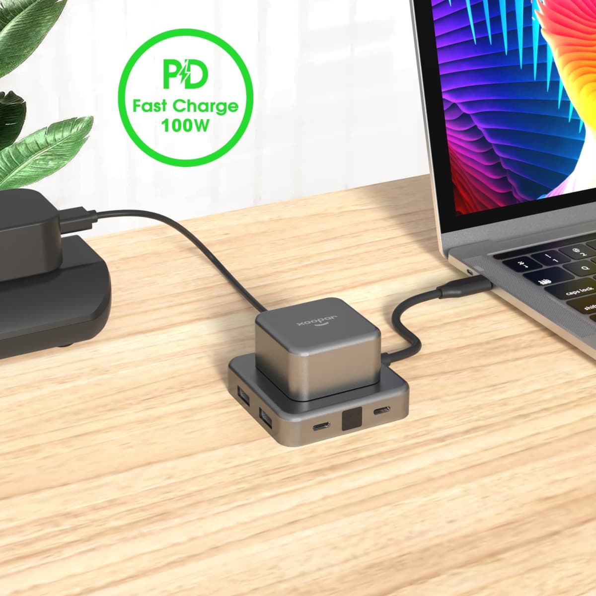 A USB hub in brushed aluminium with multiple ports, connected to a laptop on a wooden desk. Features a logo.