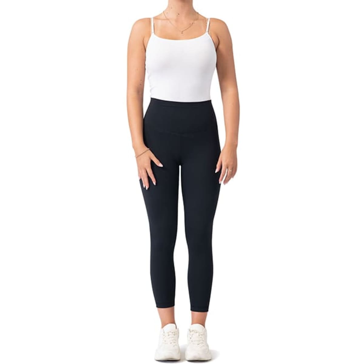 Black high-rise full-length leggings paired with a white tank top and white sneakers, featuring a logo.