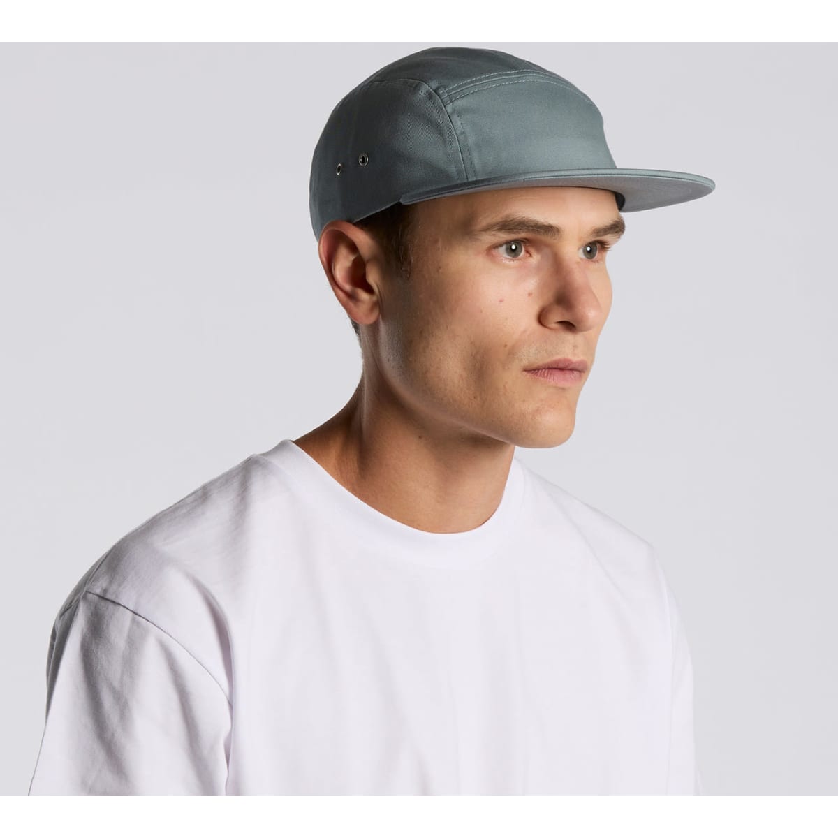 A five-panel cap in a soft blue-grey colour worn by a model, featuring a subtle logo.