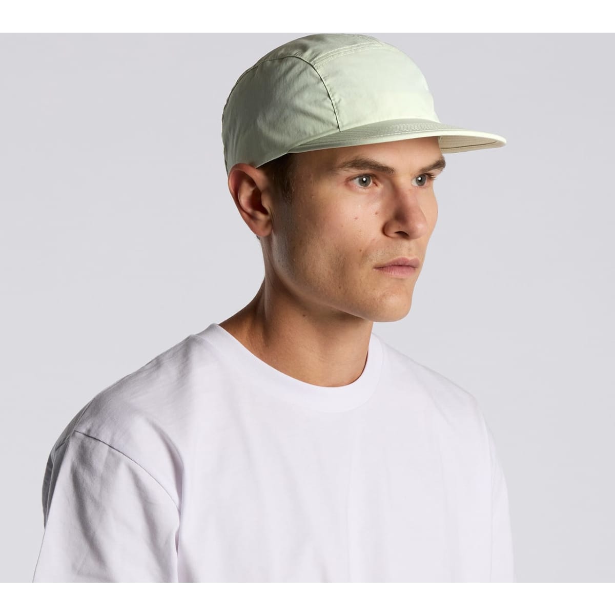 A light green nylon cap with a stiff brim, worn by a model against a plain background.