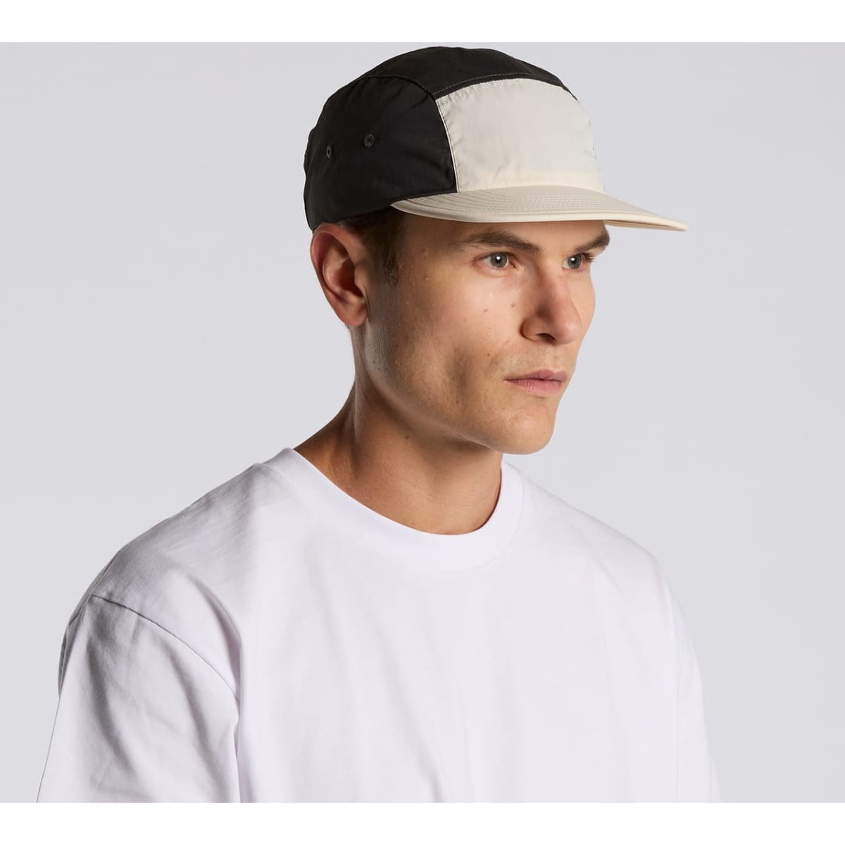 A two-tone nylon cap in black and cream, featuring a logo, worn by a model with a neutral expression.