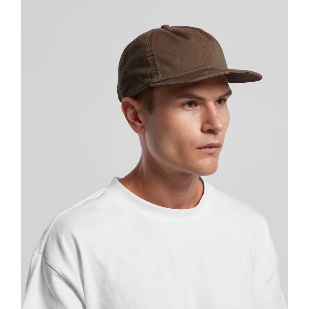 A cap in a muted brown colour worn by a model, featuring a simple design and a logo.