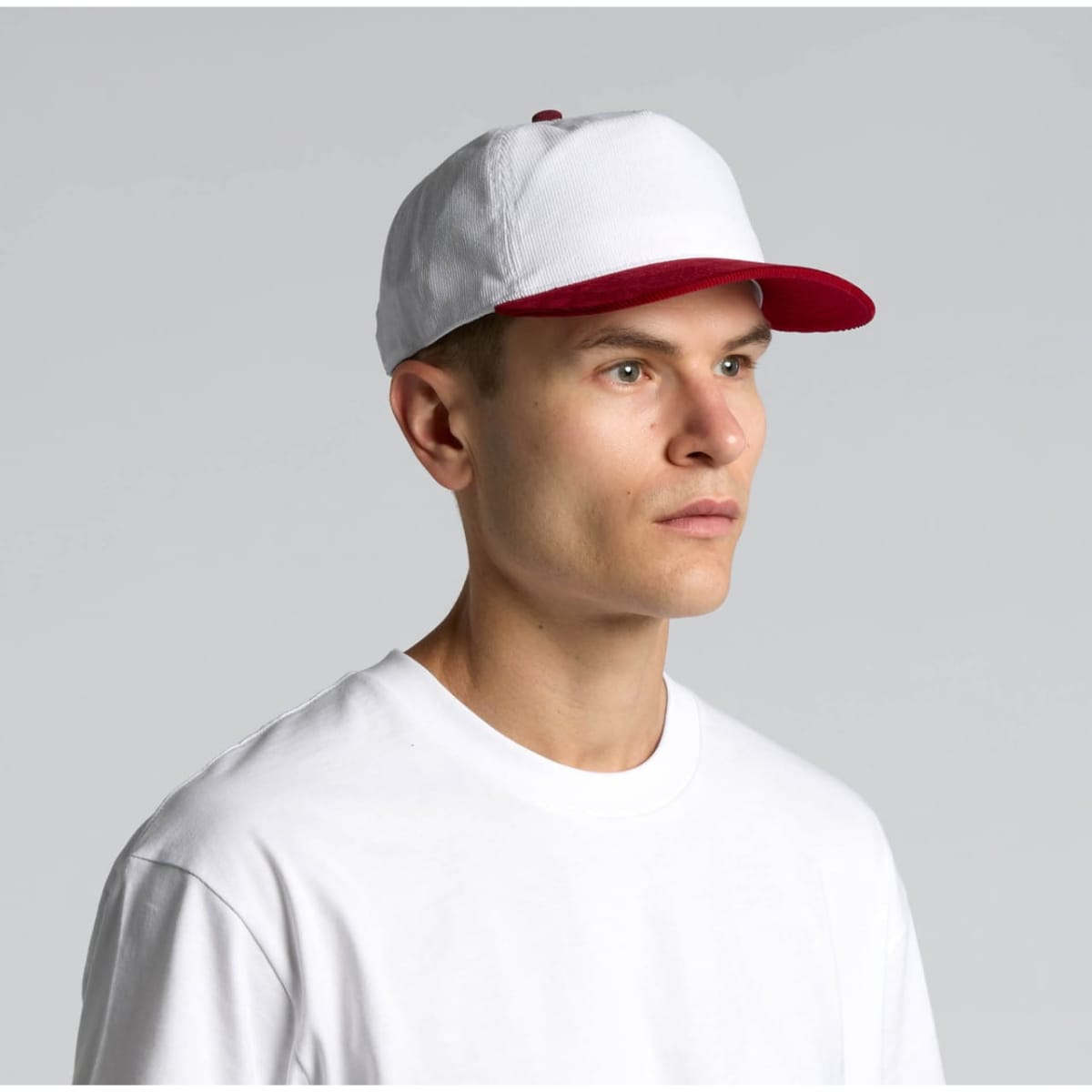A two-tone cap featuring a white crown and a red peak, worn by a model in a plain white t-shirt.