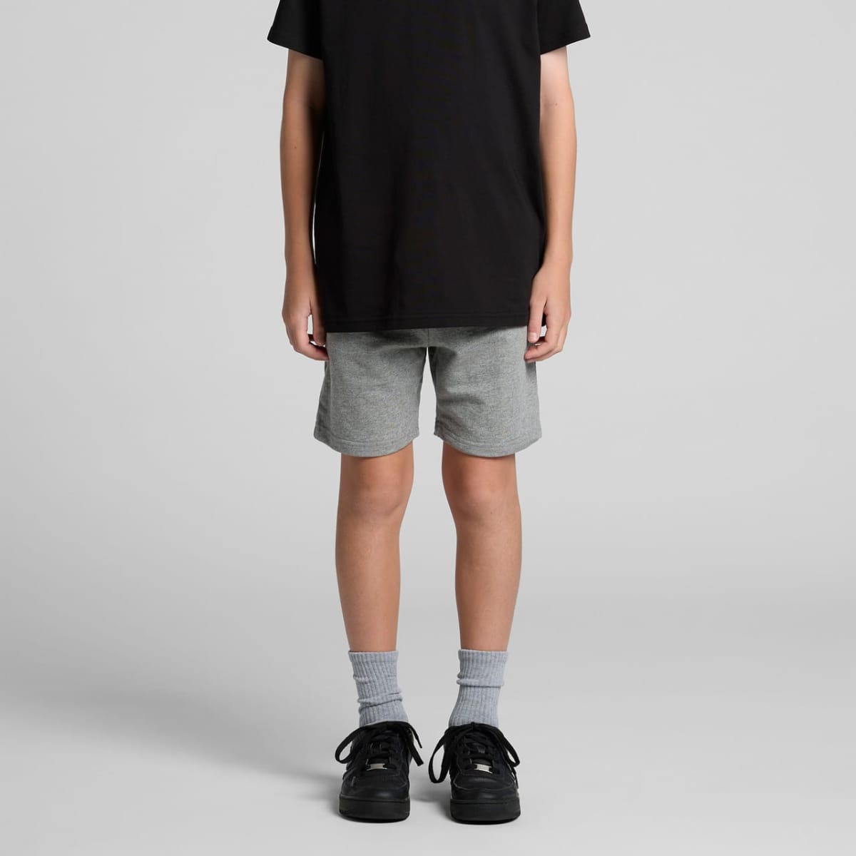 Youth stadium shorts in grey, featuring an elastic waistband, paired with black sneakers and grey socks.