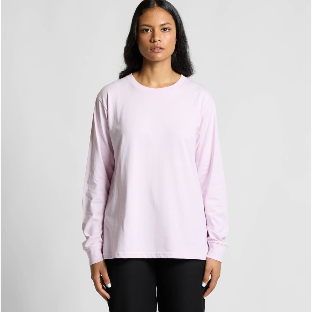 A long-sleeve T-shirt in light pink, featuring a simple design and a logo on the front. Model wears black pants.