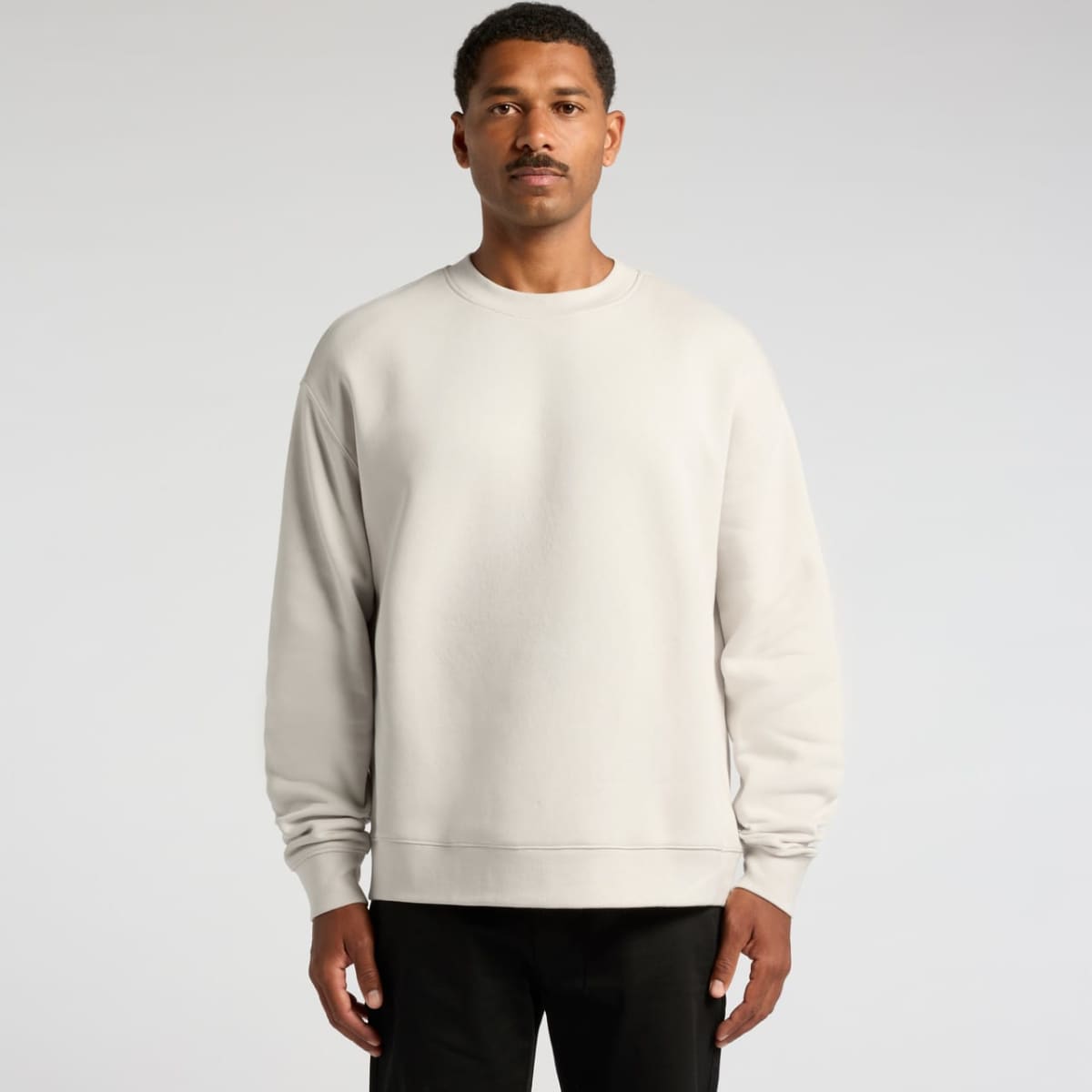 A light grey sweater on a man, featuring a relaxed fit and long sleeves. The garment has a logo on it.