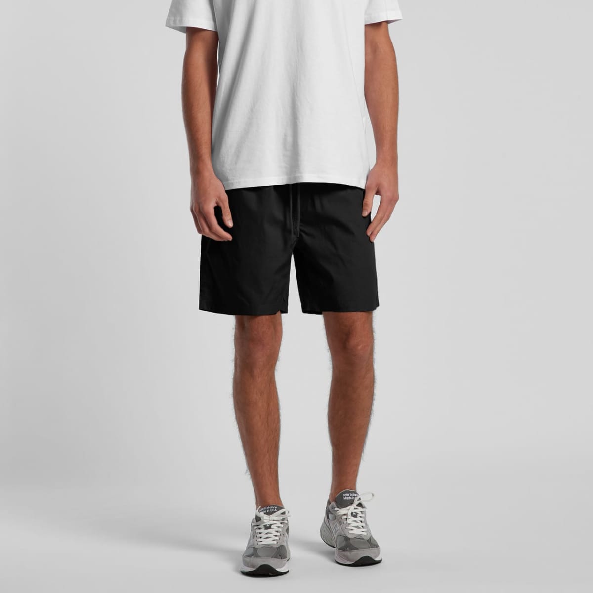 Black sports shorts with an elastic waistband, modelled by a person wearing a white t-shirt and grey sneakers.