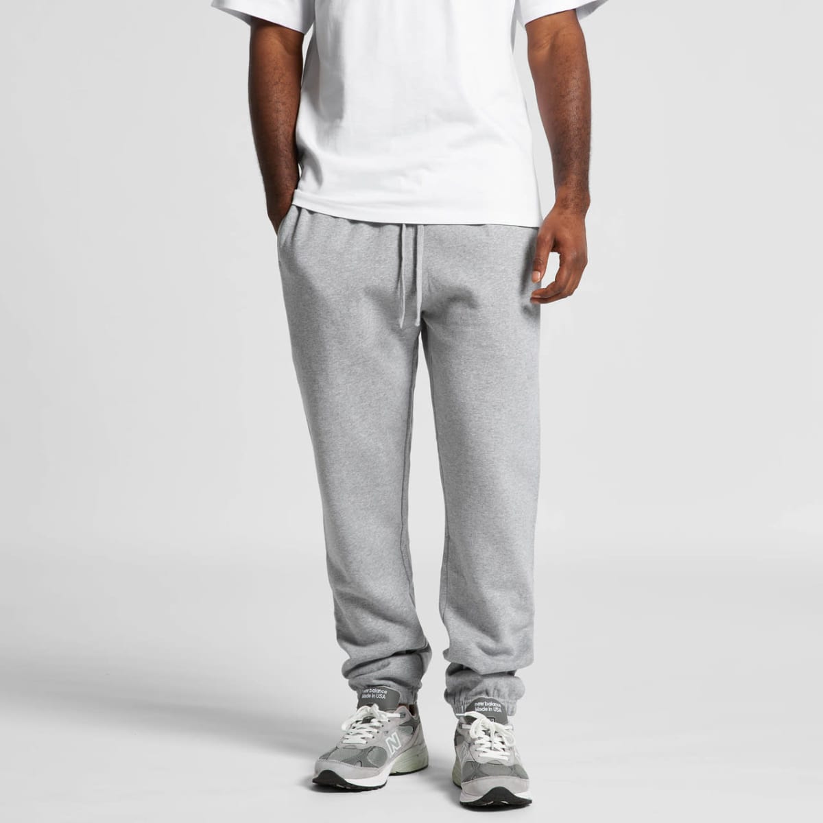 Grey track pants with elastic cuffs and a drawstring waist, worn with a white t-shirt and sneakers. Features a logo.