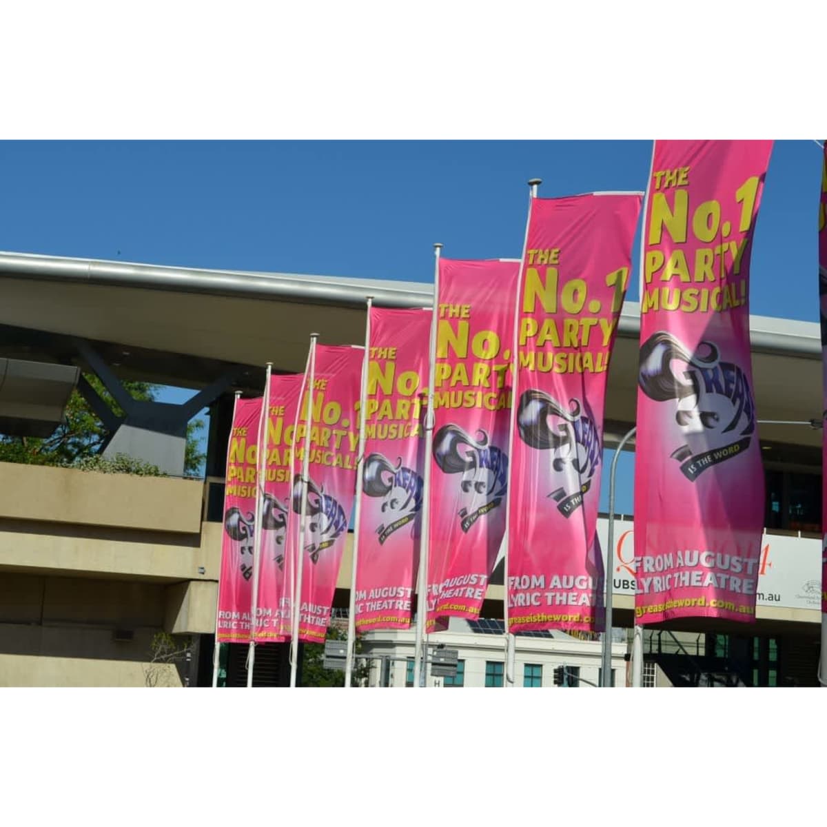 A series of pink flags featuring text and a logo, displayed outside a theatre.