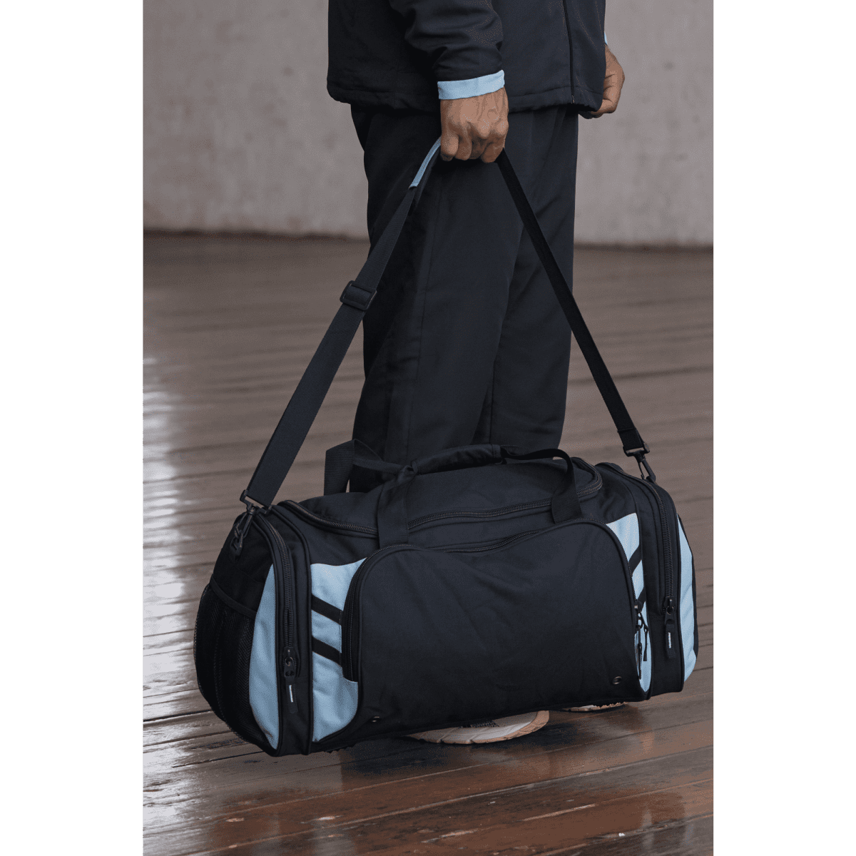 A black duffle bag with light blue accents, featuring multiple zippered pockets and a shoulder strap.
