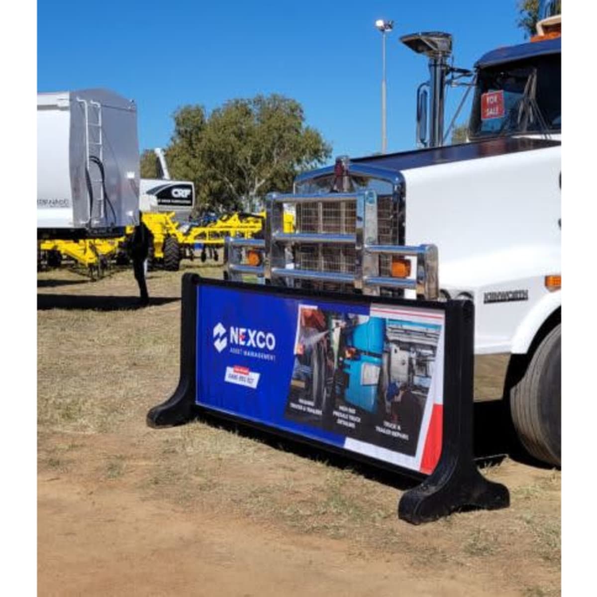 A signage barrier featuring a branded design, predominantly blue and red, displayed in an outdoor setting near equipment.