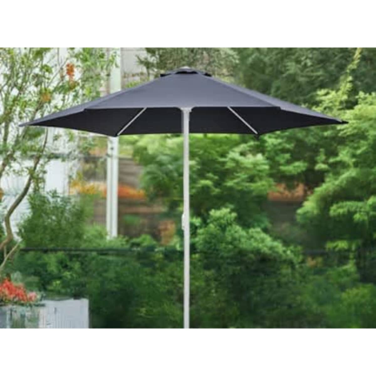 A black café umbrella with a sturdy white pole, set against a lush green garden backdrop.