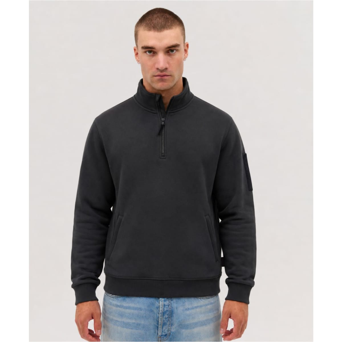 A black fleece 1/4 zip jumper with a zipper and a logo on the sleeve, worn by a model.