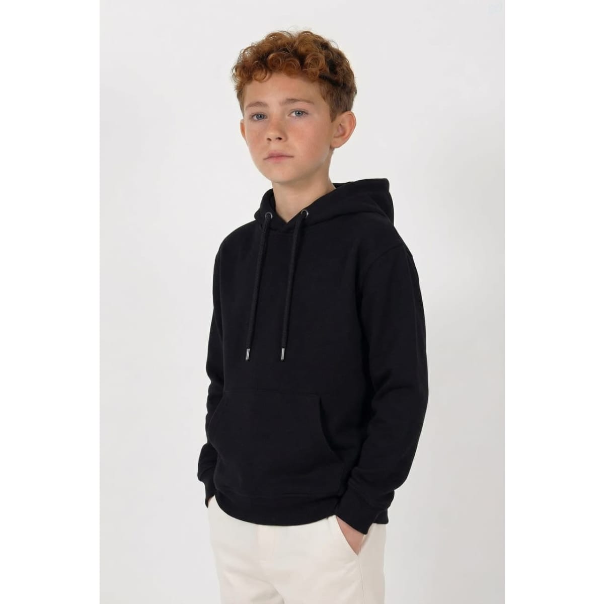A black youth hoodie featuring a front pocket and drawstring hood. The model stands with hands in pockets.