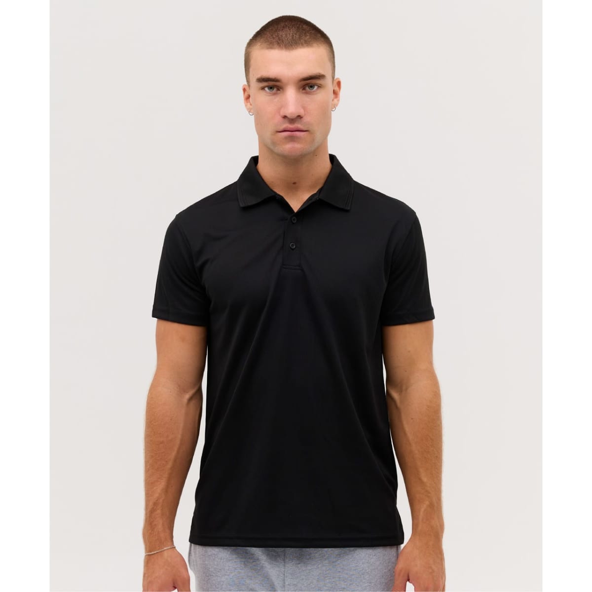 A black polo shirt displayed on a model, featuring a collar and short sleeves, with a logo on the chest.