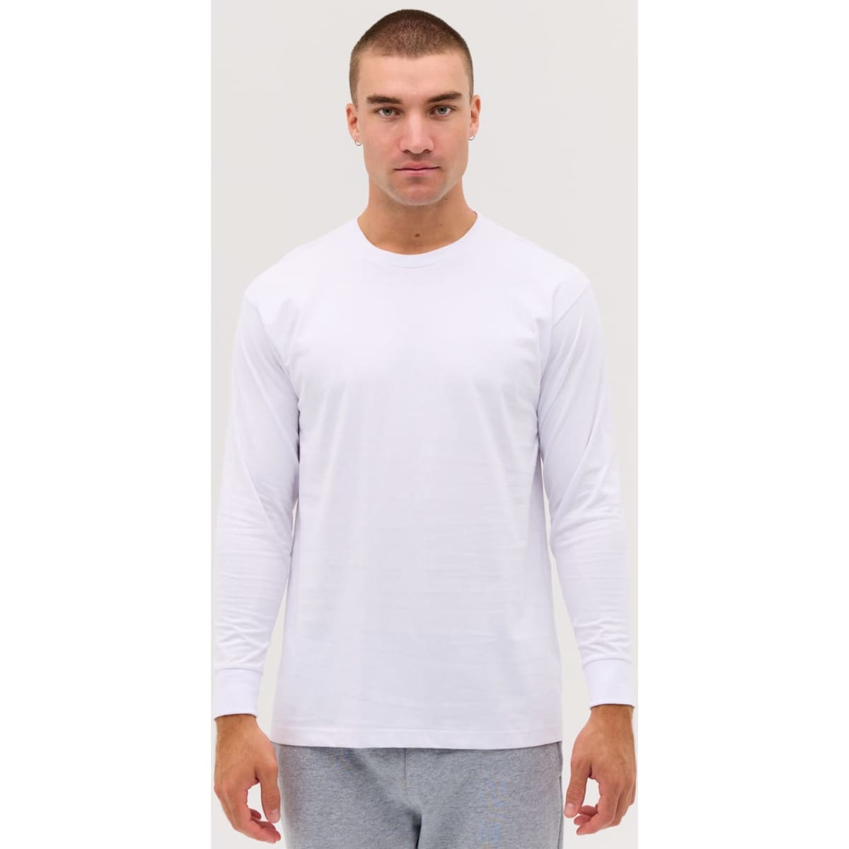 A long sleeve tee in white, featuring a classic fit and a logo on the chest. The model is wearing grey bottoms.