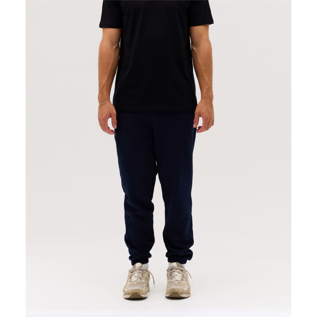 Navy track pants worn with a black t-shirt, featuring a fitted style and elasticised cuffs. The model wears beige sneakers.