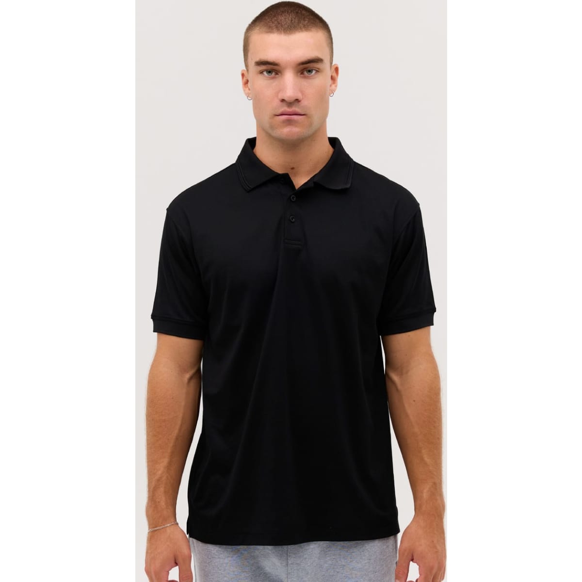 A black polo shirt is displayed on a model, featuring a collar and short sleeves. The shirt has a logo.