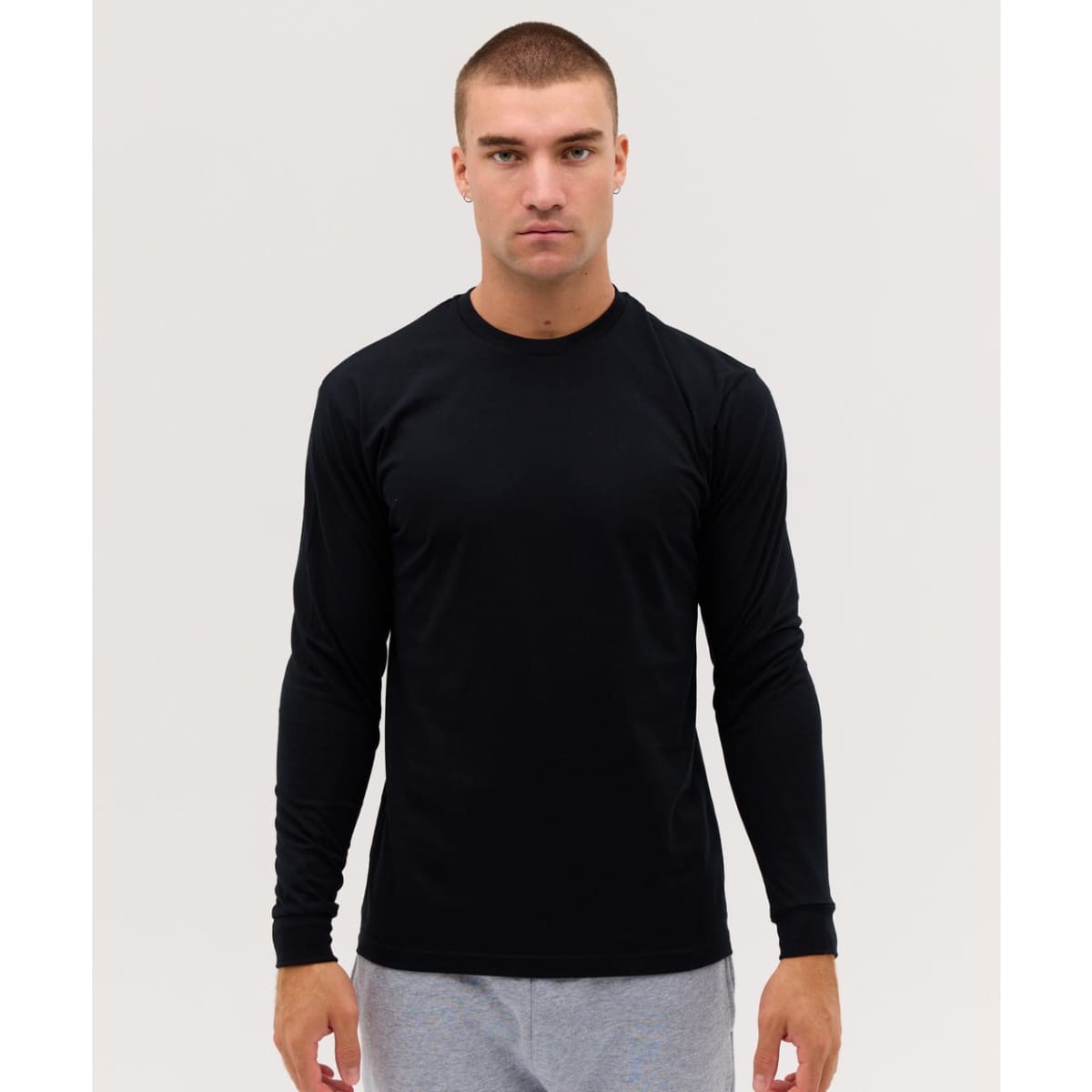 A long sleeve black tee features a fitted design and includes a logo. Model is wearing grey pants.