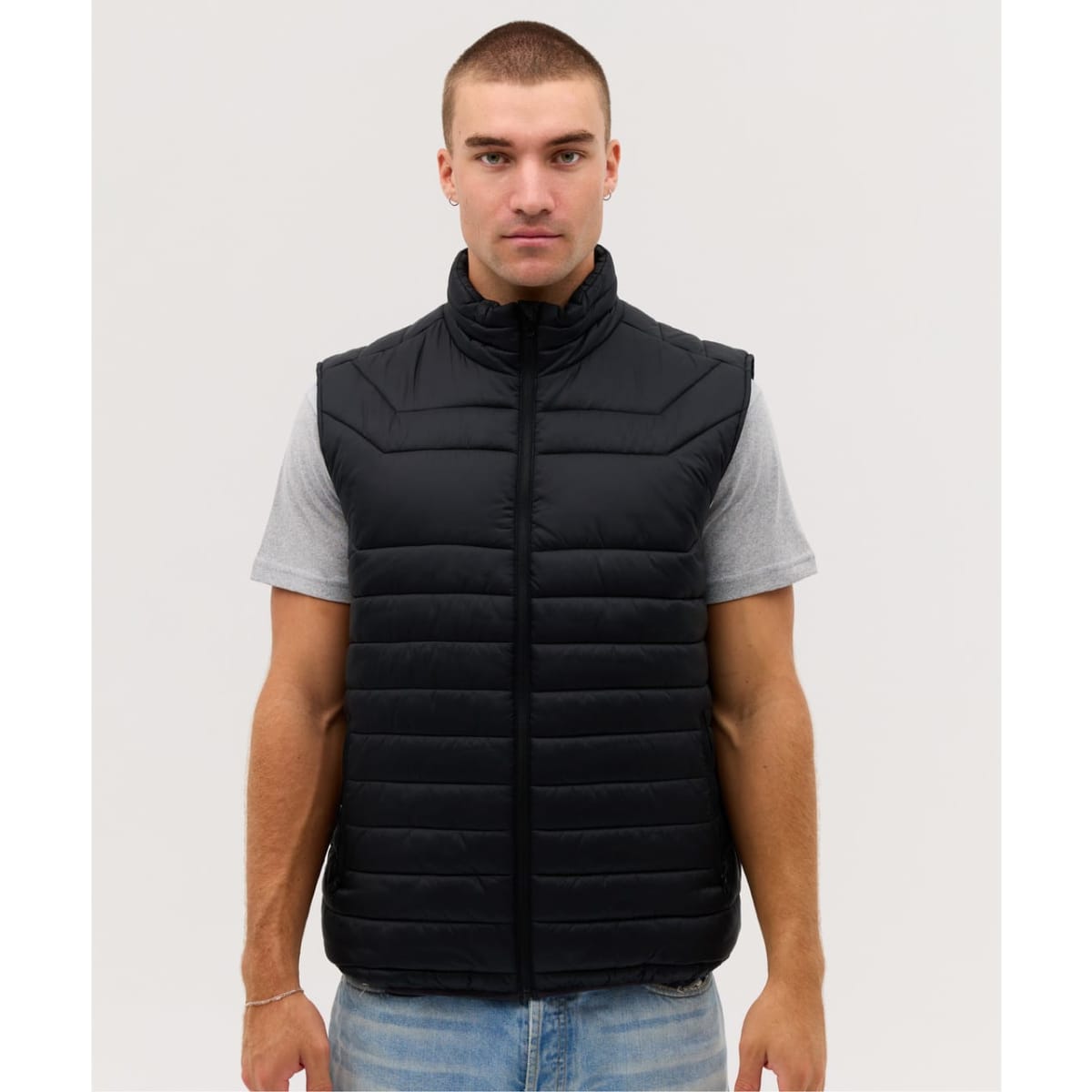 A black puffer vest is displayed, featuring a zip front and a high collar, worn over a grey T-shirt.